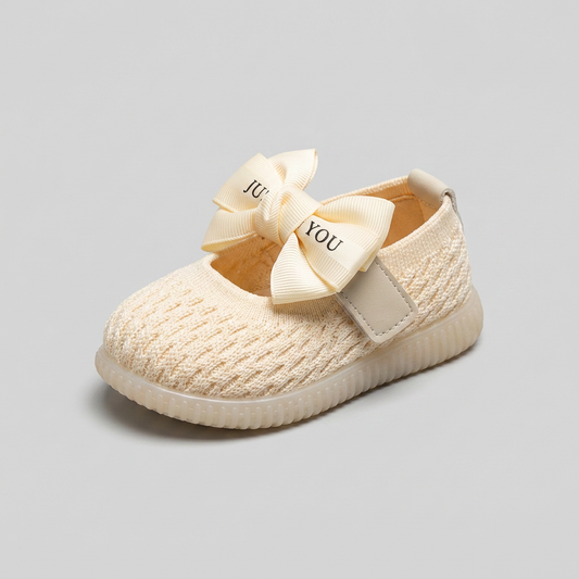 Three-quarter angle view of cream knit baby slip-on shoe with ribbon bow strap